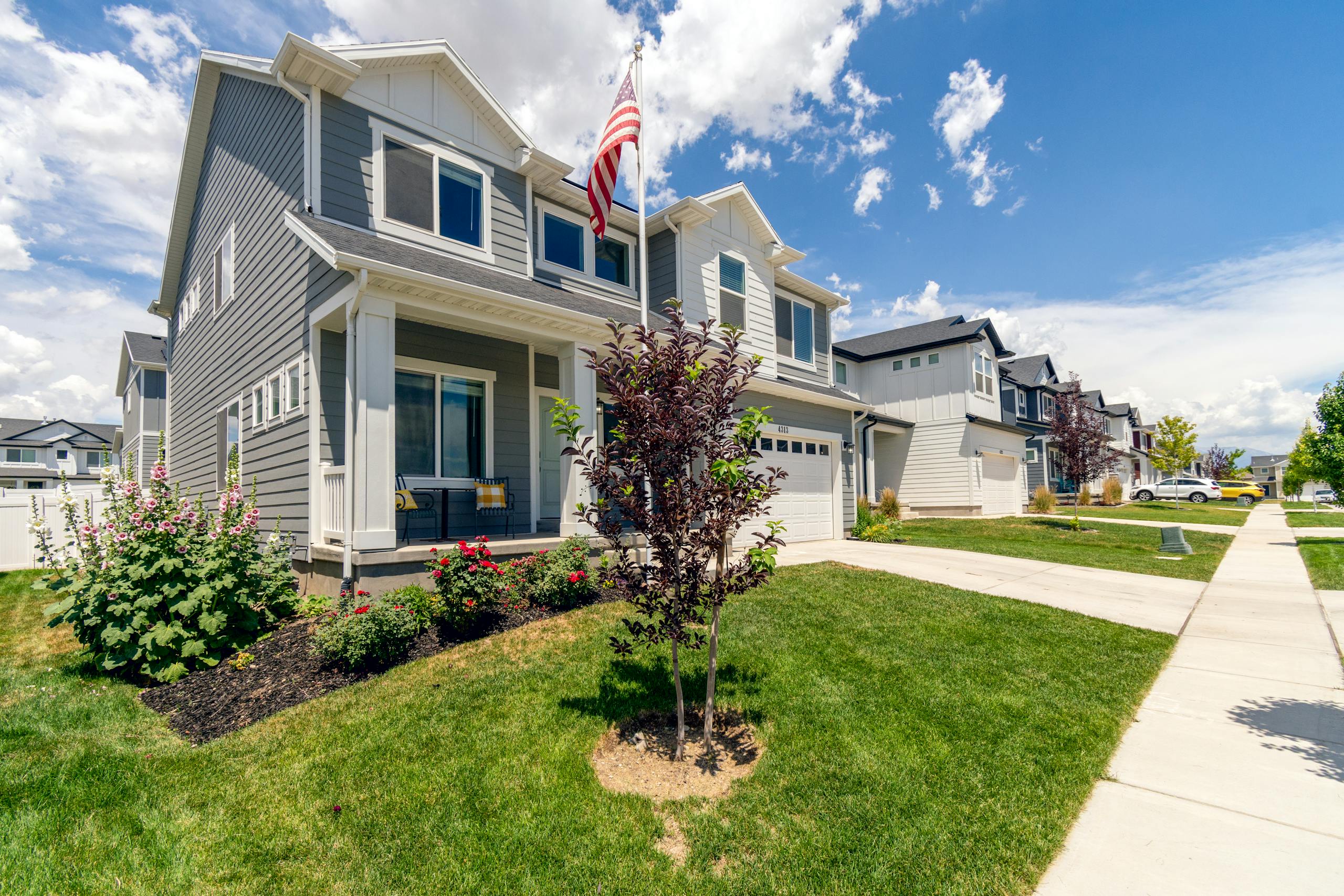 A modern suburban house with garden and American flag, showcasing beautiful architecture.